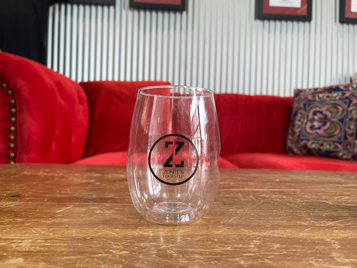 A single empty Govino polycarbonate stemless wine cup on a table with a red sofa in the background